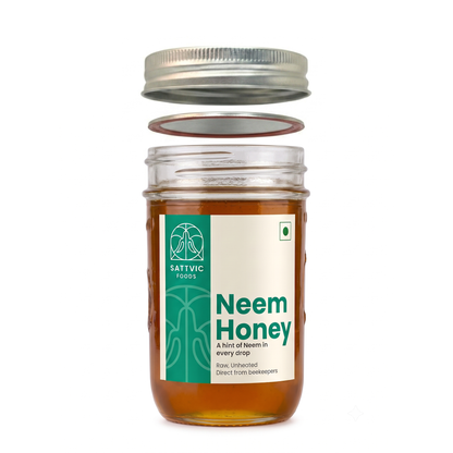 A glass jar of Satvic Foods Neem Honey with its lid removed and floating above, showing the amber-colored honey inside. The jar features a white and green label with the brand logo and product name.