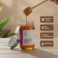Honey jar with a honey dipper, showing honey dripping, on a wooden surface with a blurred background.