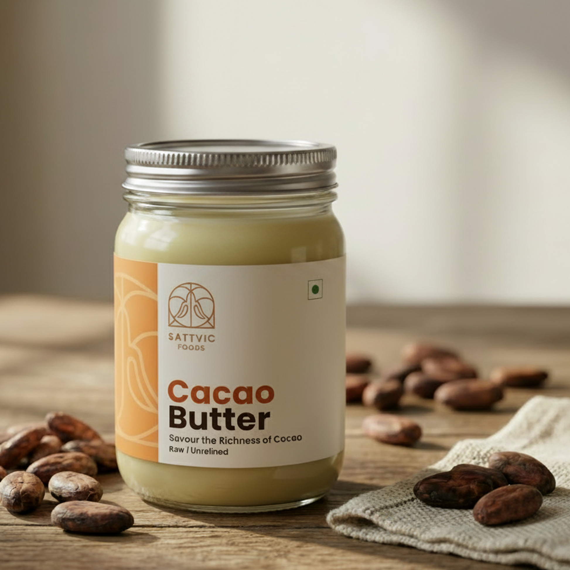 Jar of cacao butter with a label, surrounded by cocoa beans on a wooden surface.